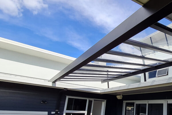 A glass pergola with metal framing partially covering a patio.