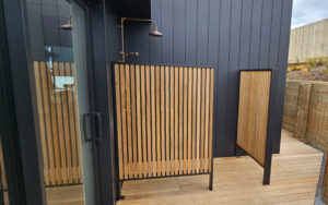 A privacy screen constructed of wood slats and metal framing installed around an outdoor shower.