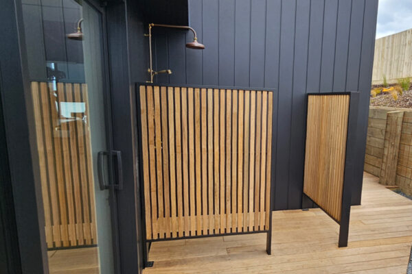 A privacy screen constructed of wood slats and metal framing installed around an outdoor shower.