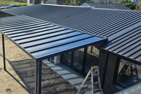 Mono-pitch pergola with black metal roofing installed over backyard area.