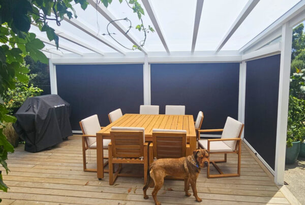 A pergola covers an outdoor dining space with a timber table and grill.